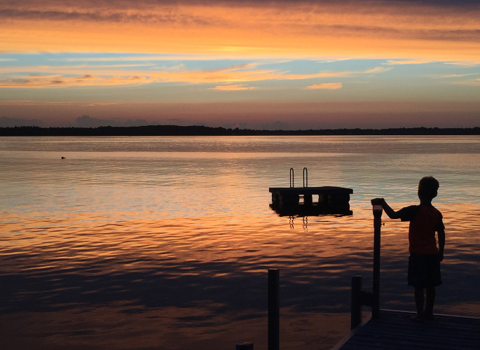 a boy looks over a lake at sunset