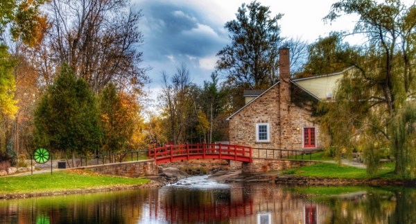 Serene landscape of Stewart Park in Perth, Ontario, featuring a charming house, vibrant red bridge, and scenic river surrounded by lush trees