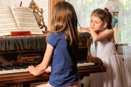 one girl plays the piano while another one listens