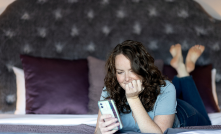 a woman browsing her phone on a hotel bed