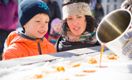 a boy and a woman are trying maple taffy