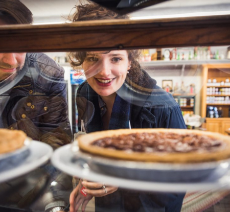 a woman looks at a pie in a bakery display case