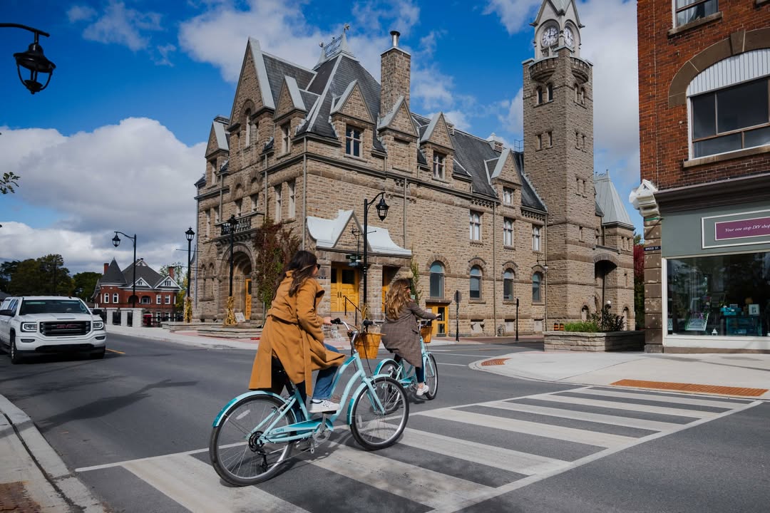People cycling through a downtown crosswalk beside a historic stone building